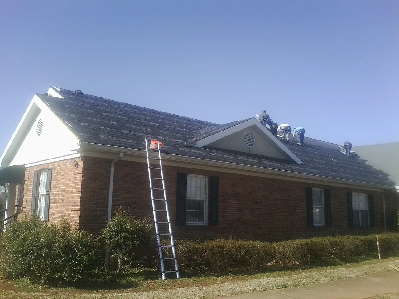 Crew tearing shingles off a brick ranch roof with a ladder set — Emergency Roof Repair work by our crew in Port Saint Joe