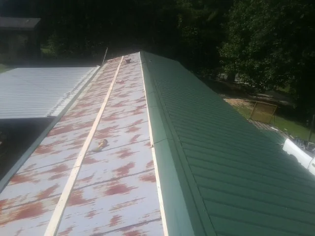 Old rusted panels beside newly installed green metal roofing — Wind Damage Roof Repair by Roofing Brothers in Port Saint Joe