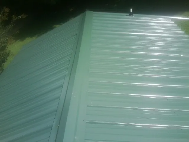New green metal panels meeting at the ridge of a roof — Flat Roof Repair work by our crew in Port Saint Joe