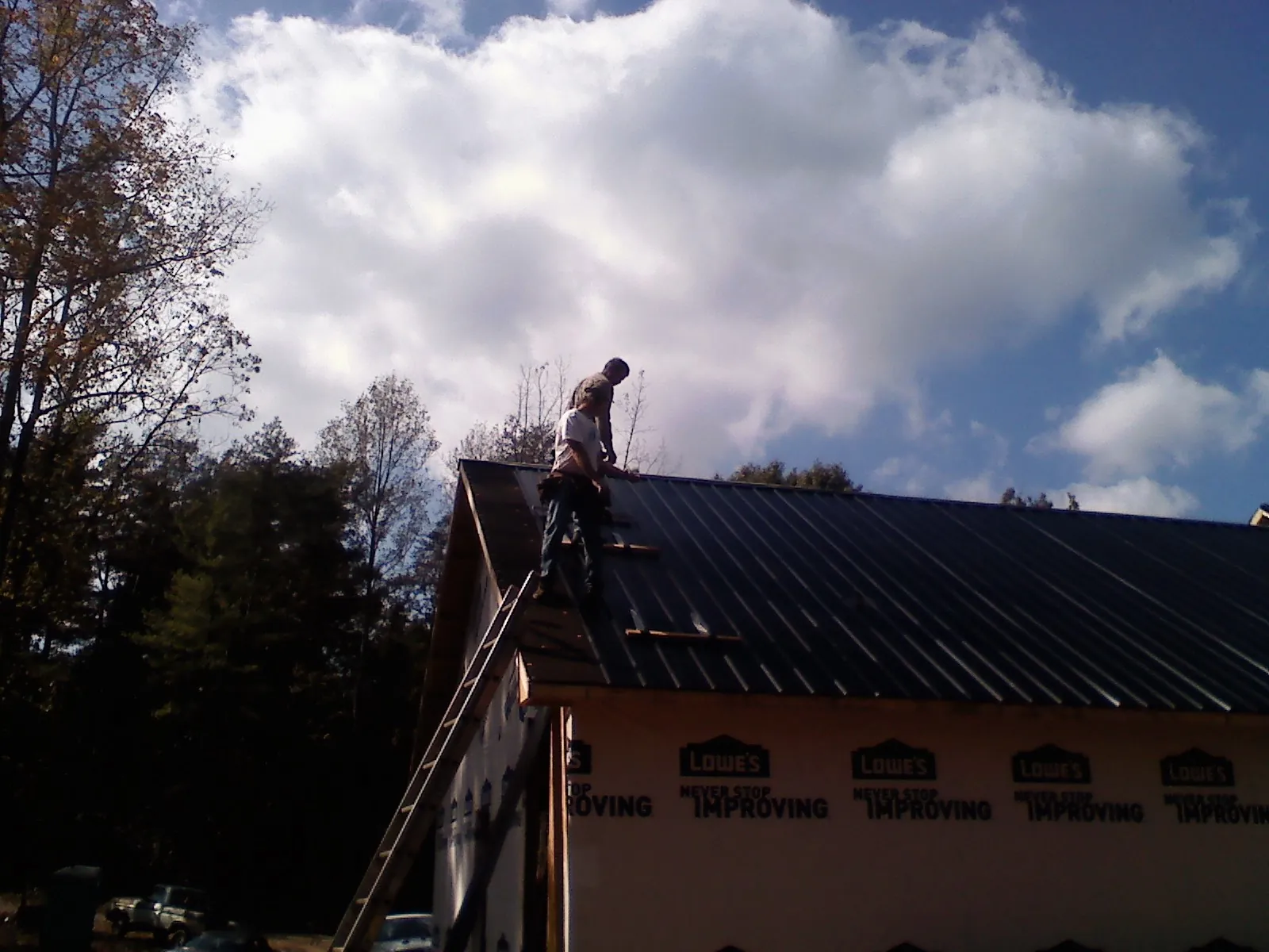 Roofer fastening dark metal panels high against a cloudy sky, from a Roof Inspection job in Port Saint Joe