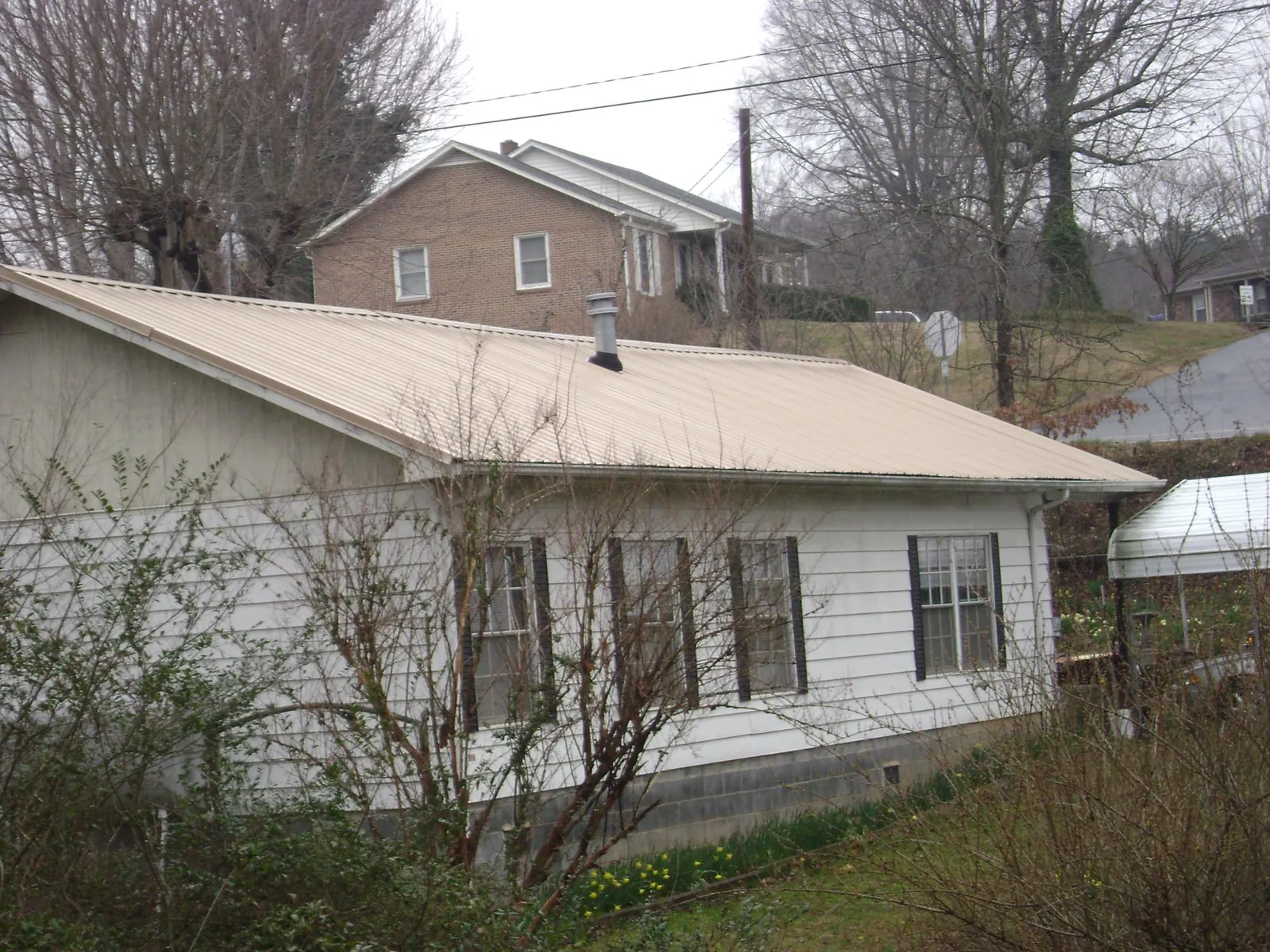 Tan metal roof on a white sided house set into a hillside — Commercial Roofing by Roofing Brothers in Port Saint Joe