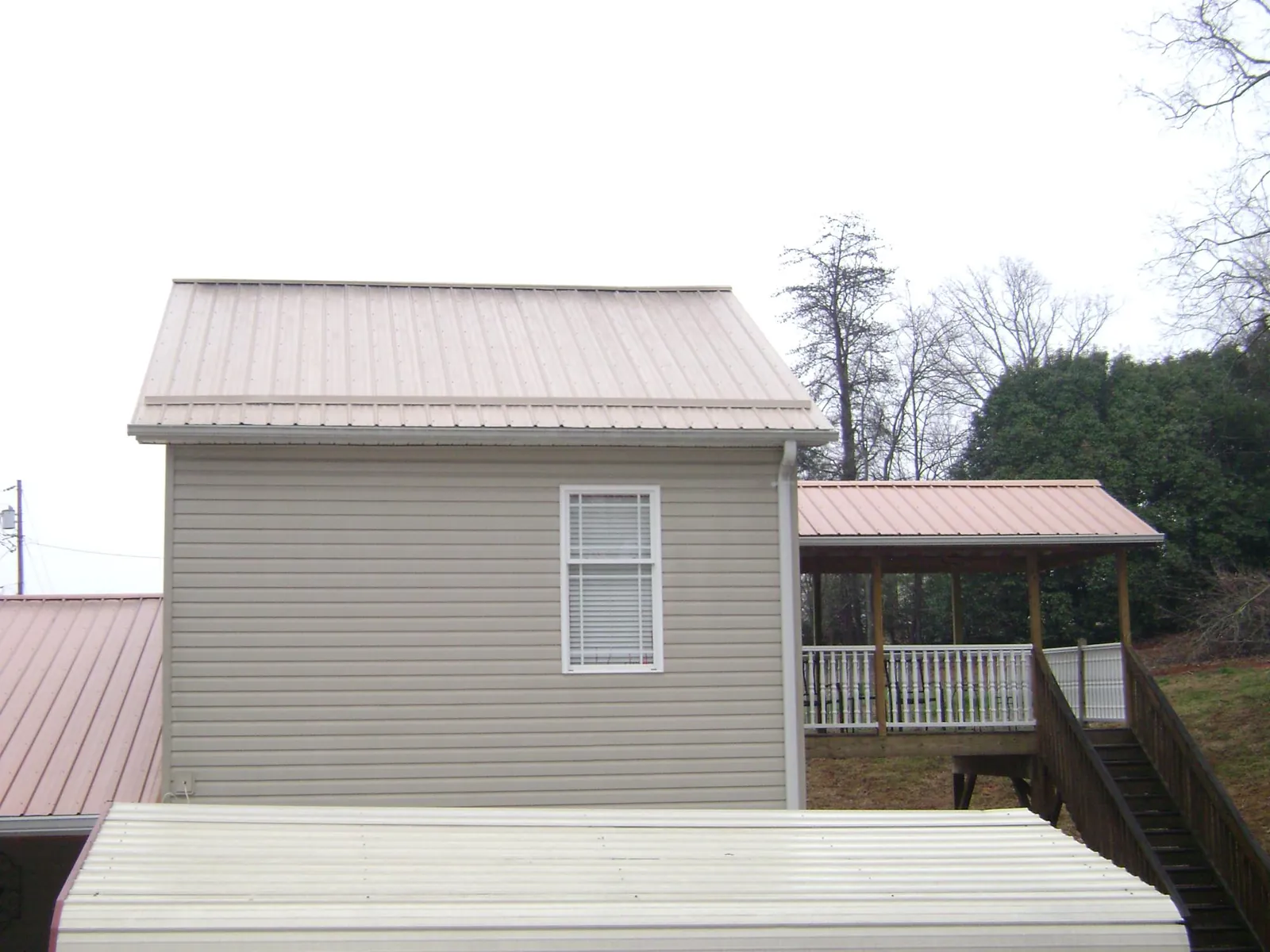 Tan metal roofs on a two story addition and attached porch, from a Roof Replacement job in Port Saint Joe